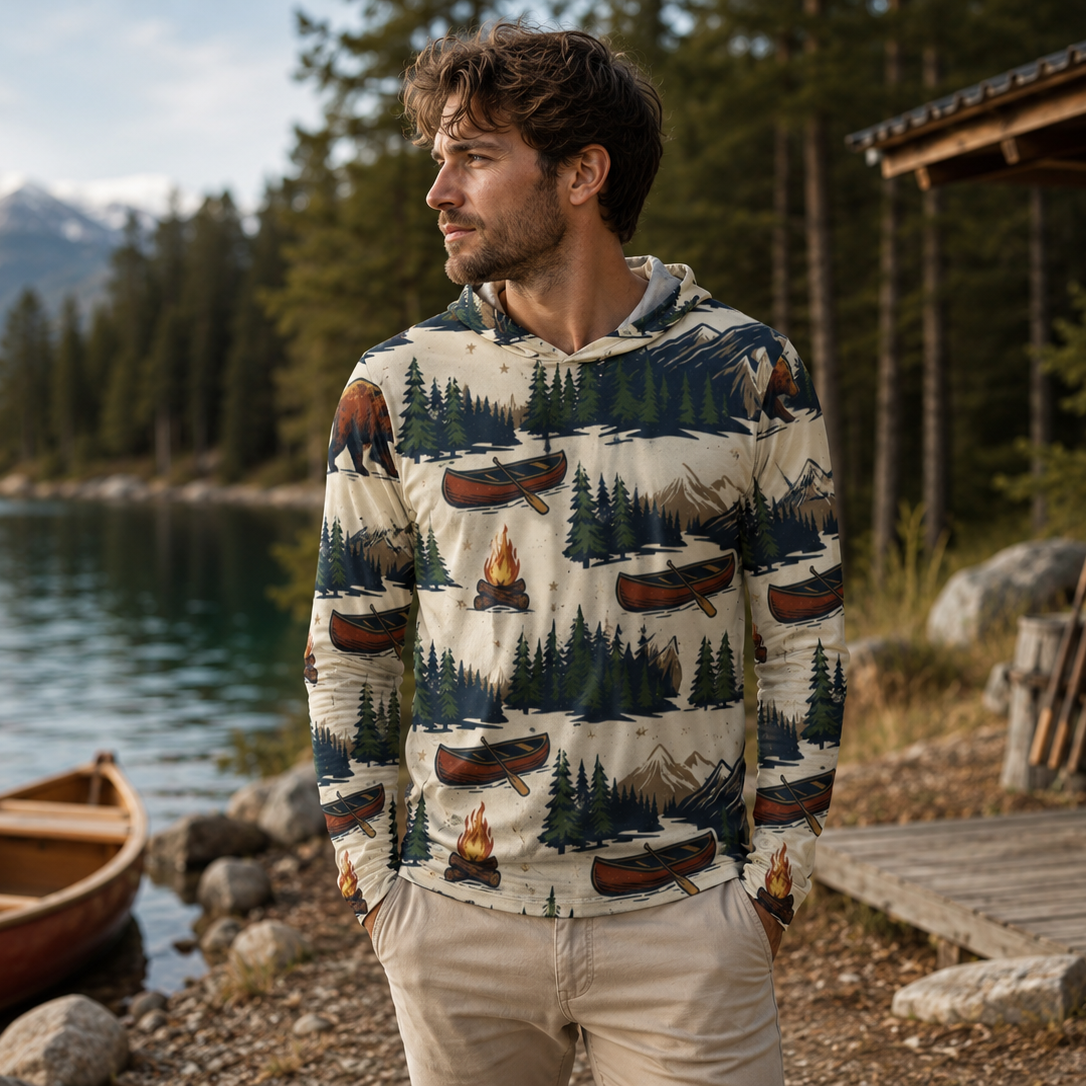 Man wearing a patterned hoodie by a lake with mountains in the background